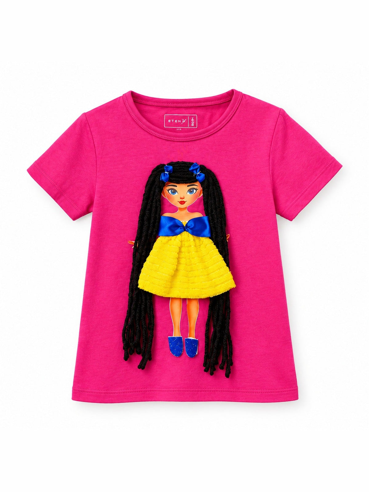 Pink girls T-shirt with handmade doll appliqué featuring long black yarn hair with blue bows, yellow textured dress with blue satin bow, and blue sparkle shoes, flat product photo