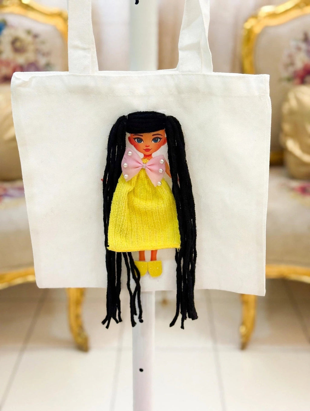 White canvas tote bag with handmade doll appliqué featuring long black yarn hair in pigtails, pink pearl bow, yellow textured dress, and yellow shoes
