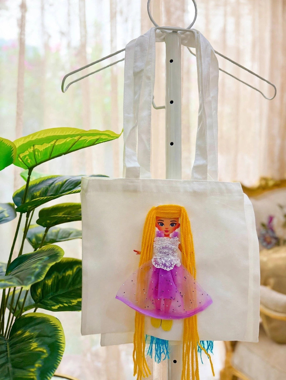 White canvas tote bag with handmade doll appliqué featuring long golden-blonde yarn hair, white lace bodice, purple sparkle tulle skirt, and yellow shoes