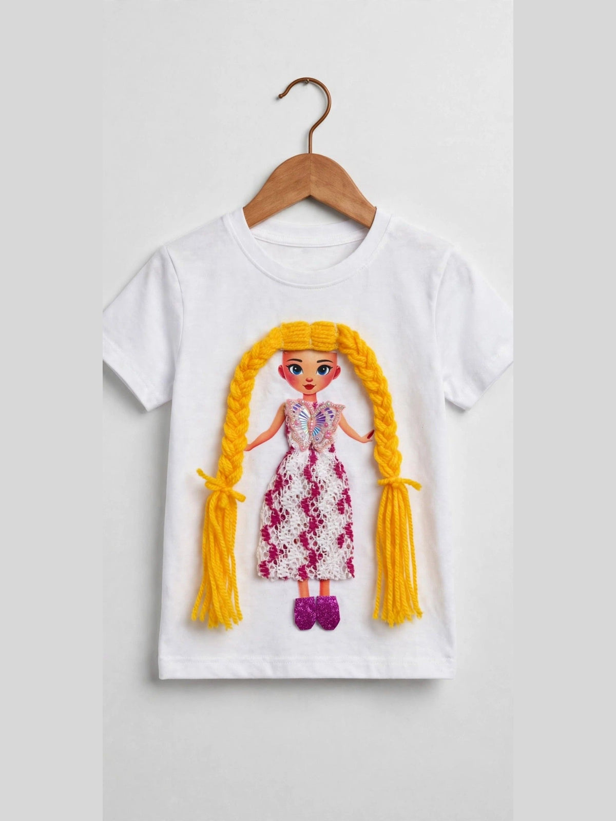 Styled photo of white girls T-shirt on pearl hanger with 3Sisters Fashion branding, featuring handmade doll appliqué with long yellow braided hair and pink floral lace dress