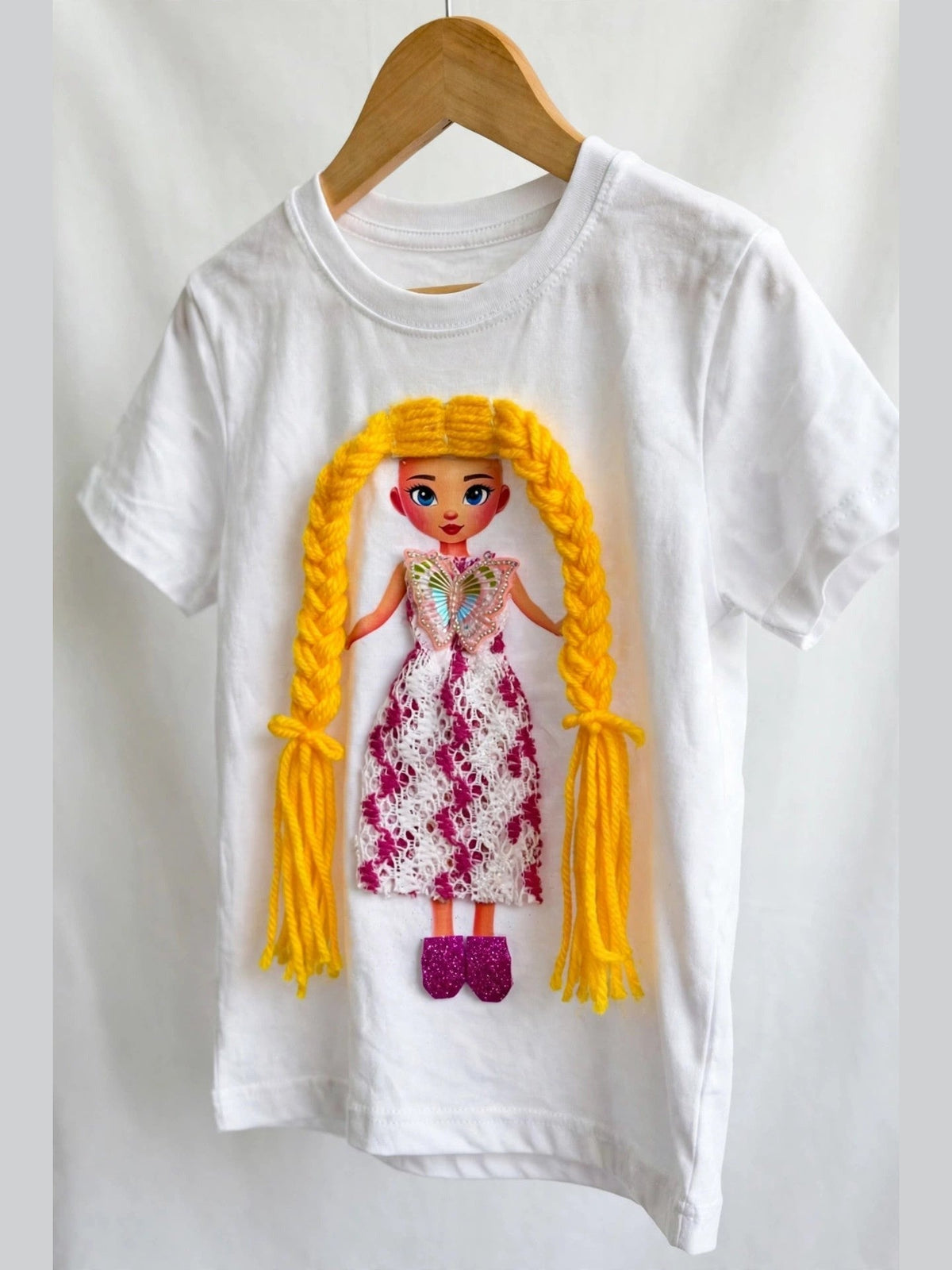 White girls T-shirt on wooden hanger with handmade yellow-haired doll appliqué in pink and white floral lace dress with butterfly bodice