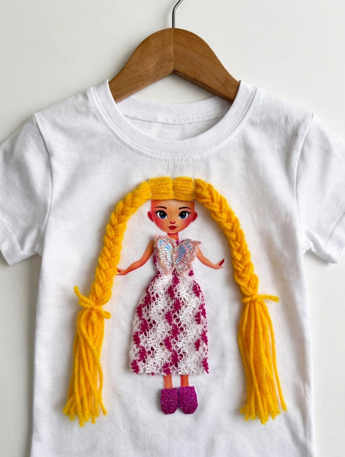 Closer view of handmade doll appliqué on white T-shirt showing yellow braided yarn hair and floral lace dress detail